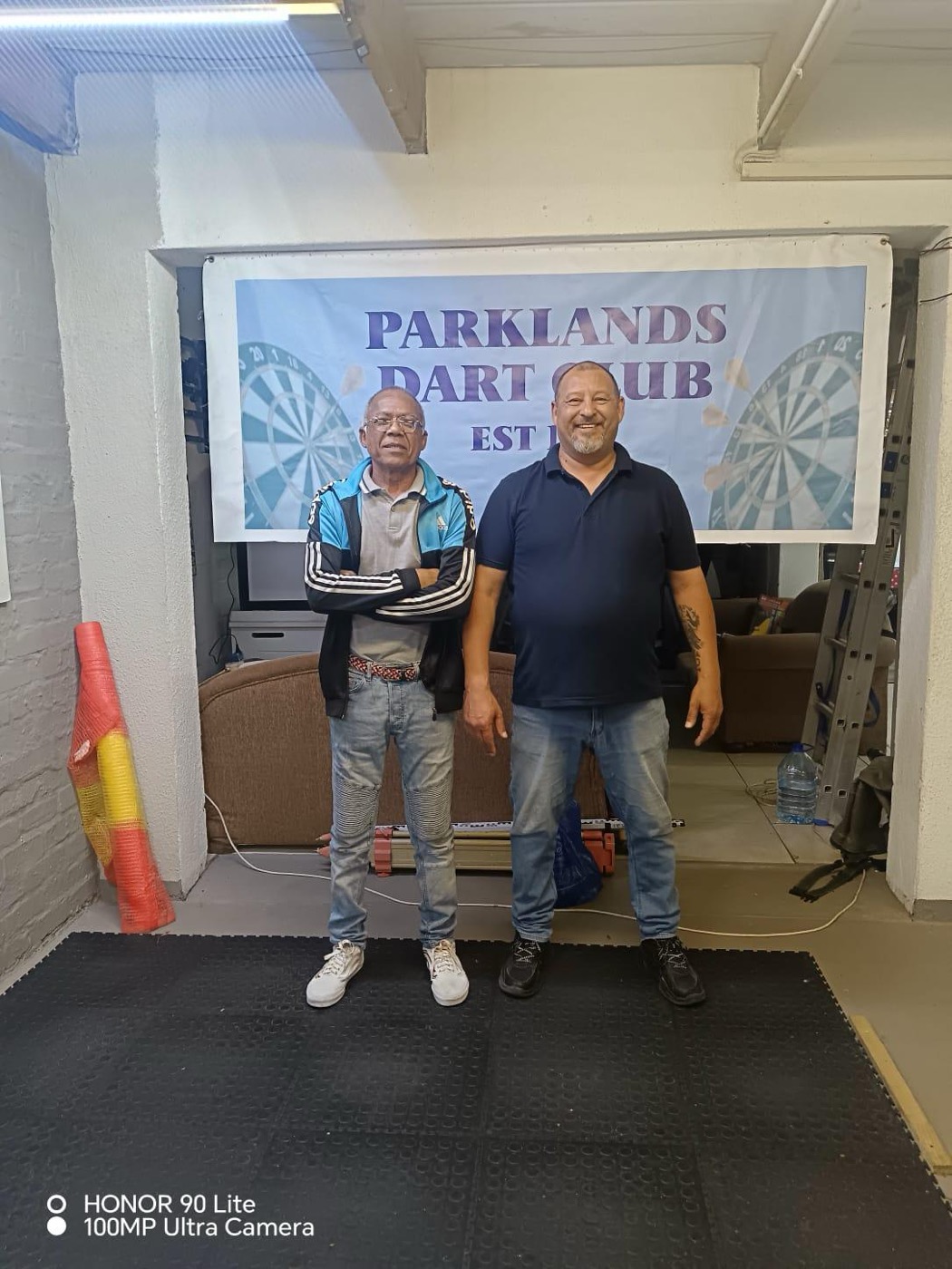 Two club members standing in front of the Parklands Dart Club banner